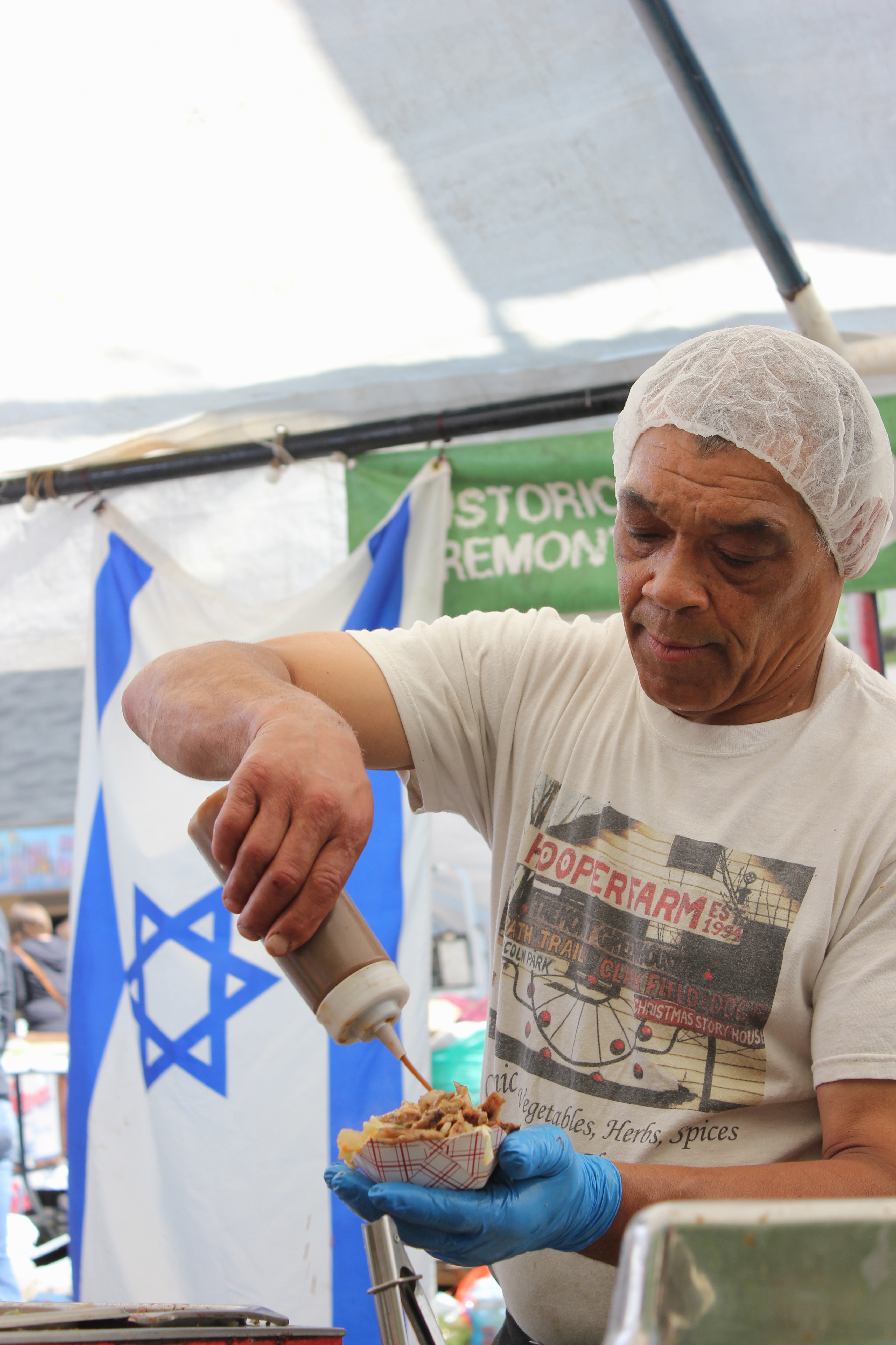 With an Israeli flag hanging at his food tent, Erich Hooper prepares a dish for a customer at the 2016 Hessler Street Fair.