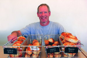 Bialy’s Bagels owner Mark Osolin stands behind his finished products, while other bagels rest in various stages of production, from baking in the oven to cooling on the pan.