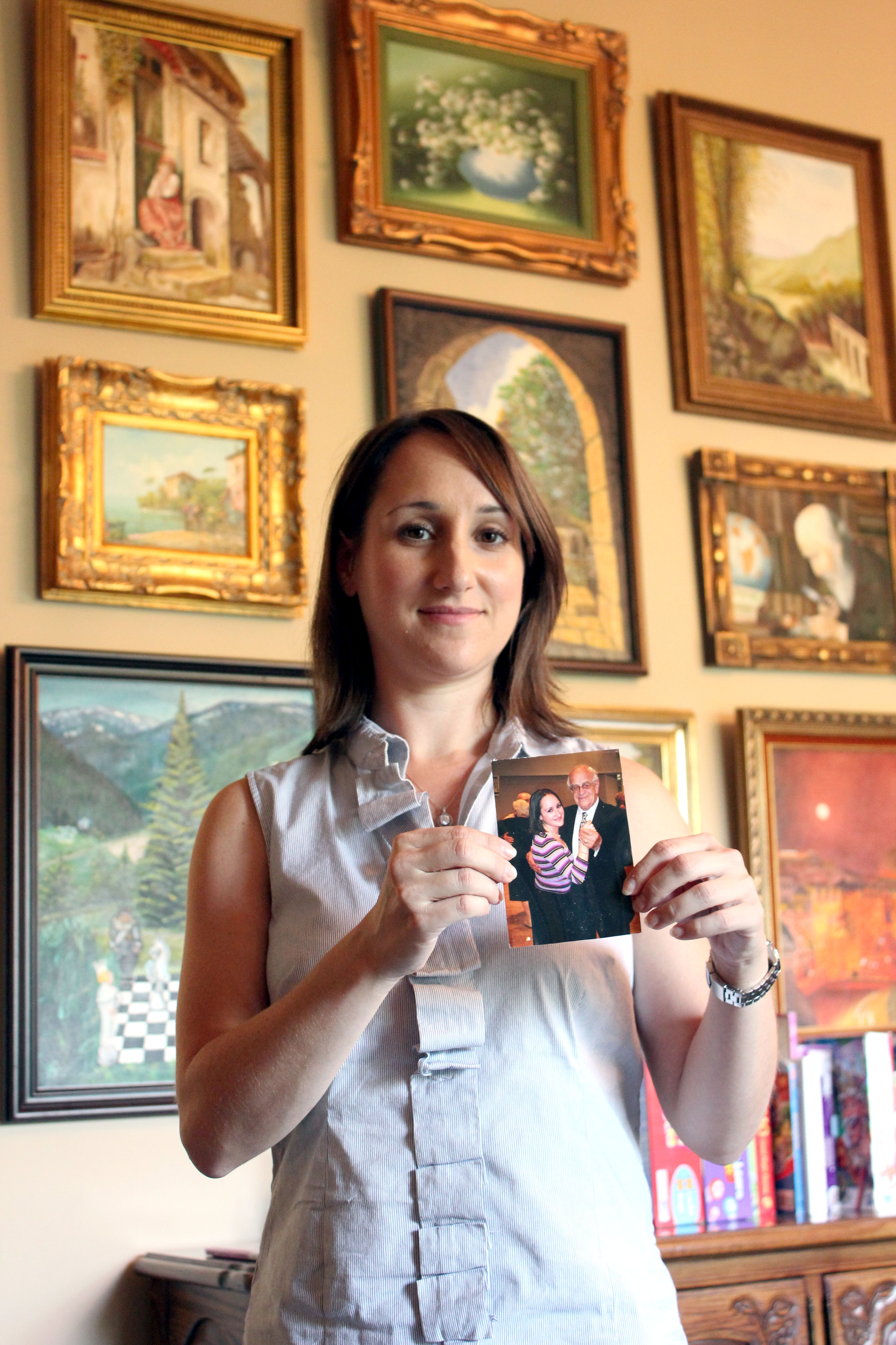 Julie Kronenberg holds a photo of her dancing with her grandfather, Jacob Hennenberg, a Holocaust survivor during a 2001 Kol Israel dinner held in honor of him. Behind her are several of her grandfather’s paintings, and the Beachwood house in which she now lives was once her grandparents’ home.