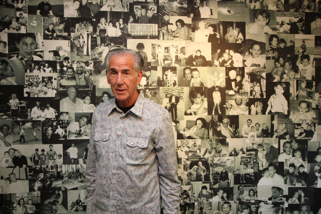 Art collector Mike Belkin in front of a wall-sized photo collage his wife, Annie, assembed. The collage, located on the lower level of the couple’s Geauga County home, includes pictures of familly and friends.
